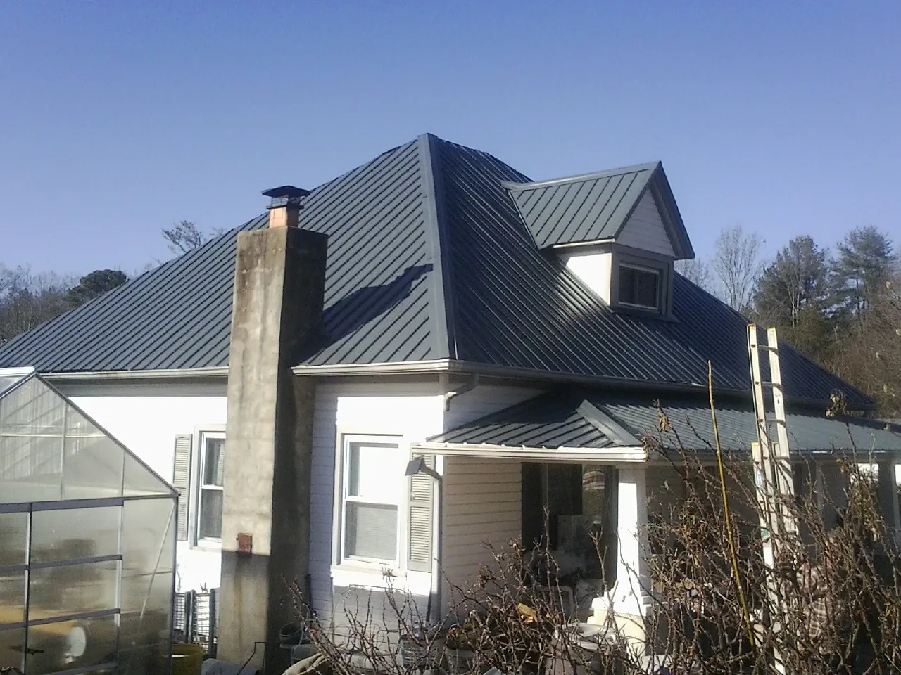 Dark blue standing seam metal roof on a white farmhouse with dormer — Slate & Tile Roof Repair by Roofing Brothers in Mont Clare