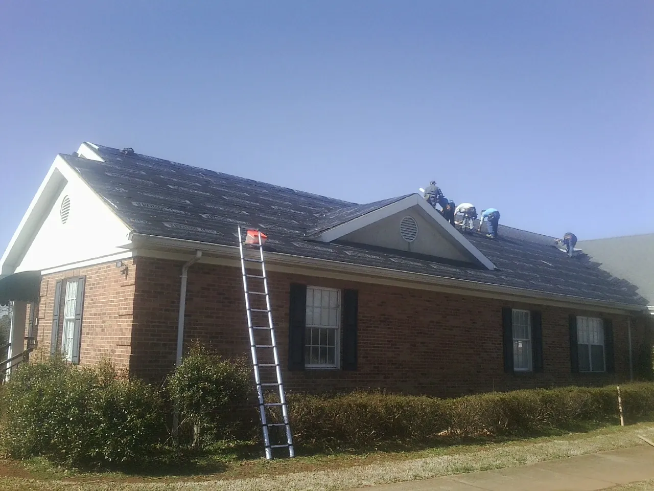Crew tearing shingles off a brick ranch roof with a ladder set — Metal Roof Repair work by our crew in Mont Clare