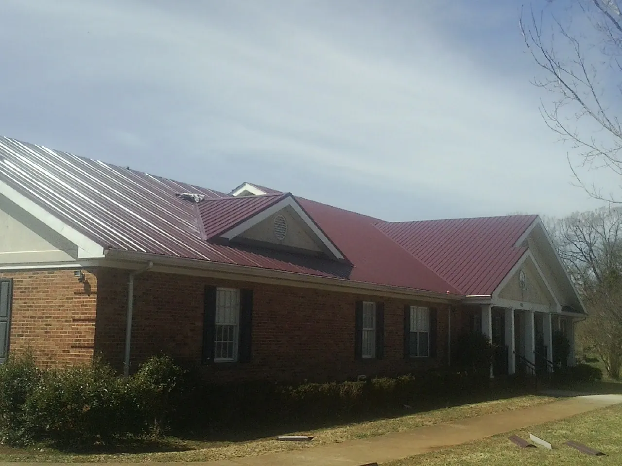 Red metal roof with gabled entries on a long brick building, from a Hail Damage Roof Repair job in Mont Clare