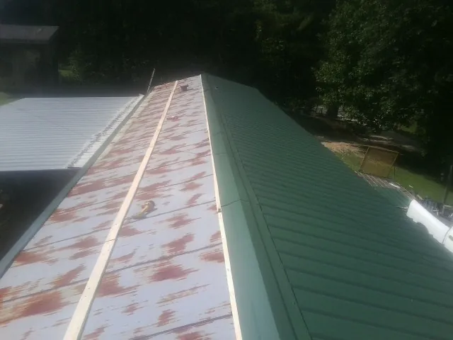 Old rusted panels beside newly installed green metal roofing — Wind Damage Roof Repair by Roofing Brothers in Mont Clare