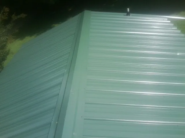 New green metal panels meeting at the ridge of a roof — Flat Roof Repair work by our crew in Mont Clare
