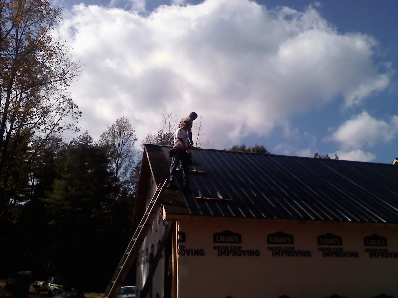 Roofer fastening dark metal panels high against a cloudy sky, from a Roof Inspection job in Mont Clare