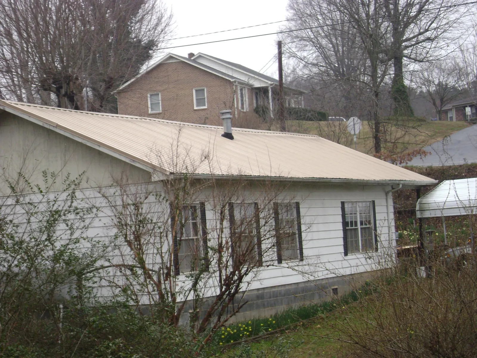 Tan metal roof on a white sided house set into a hillside — Commercial Roofing by Roofing Brothers in Mont Clare